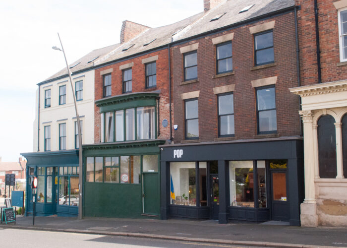170–175 High Street West, Sunderland in 2022. An oblique view of three shopfronts from across the street. From left to right, a turquoise shopfrint with an A-frame sign outside; a dark green shopfrint with a curved bay window above, and a dark grey shopfront with the word POP in large white letters at upper left. Part of a fourth building neoclassical frontage with decorated columns is at the far right. 